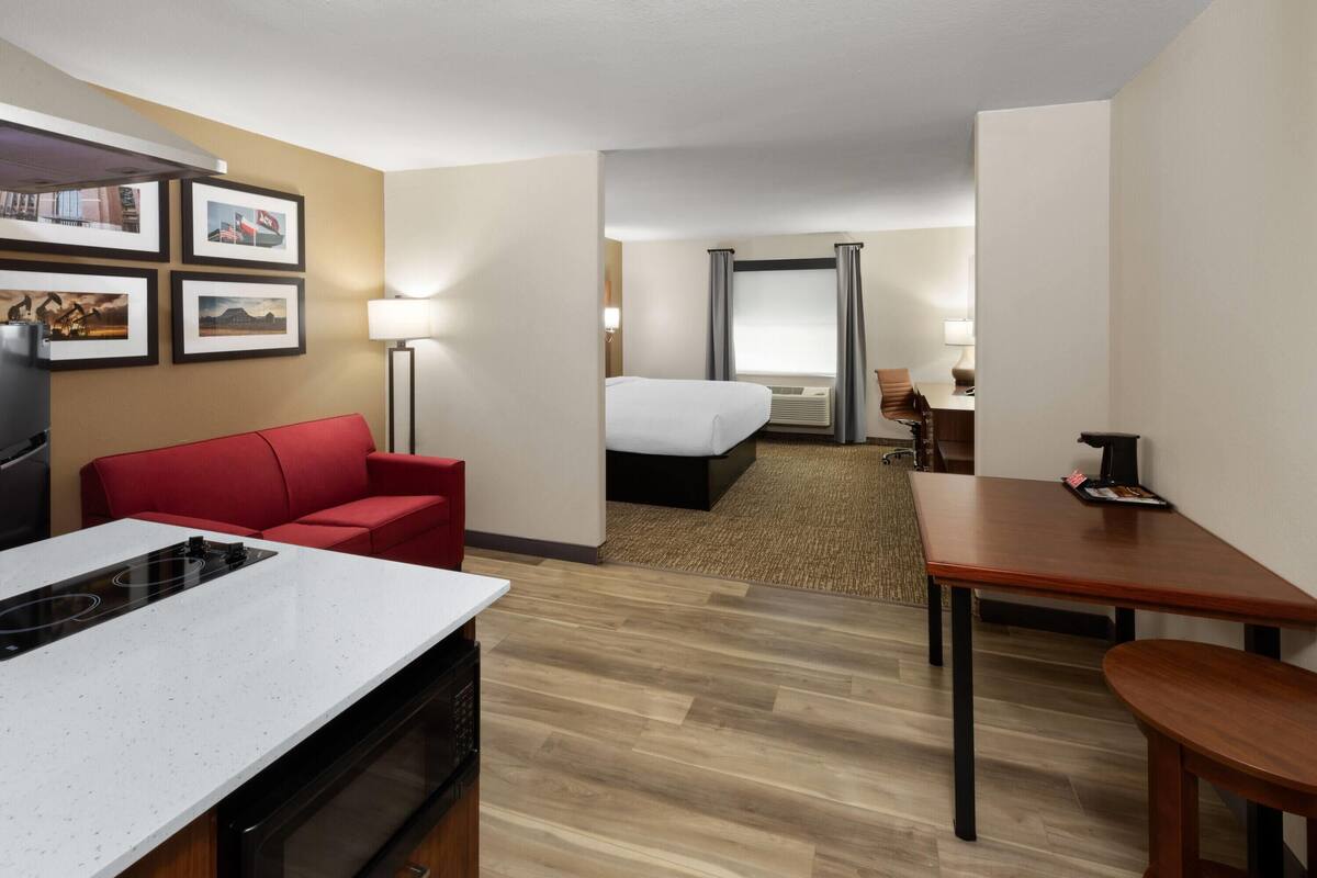 A hotel room with a kitchenette, a red sofa, a bed, a wooden table, and a desk.