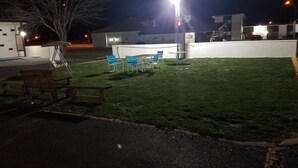 An outdoor area with a grassy lawn, a white wall, and a few chairs.