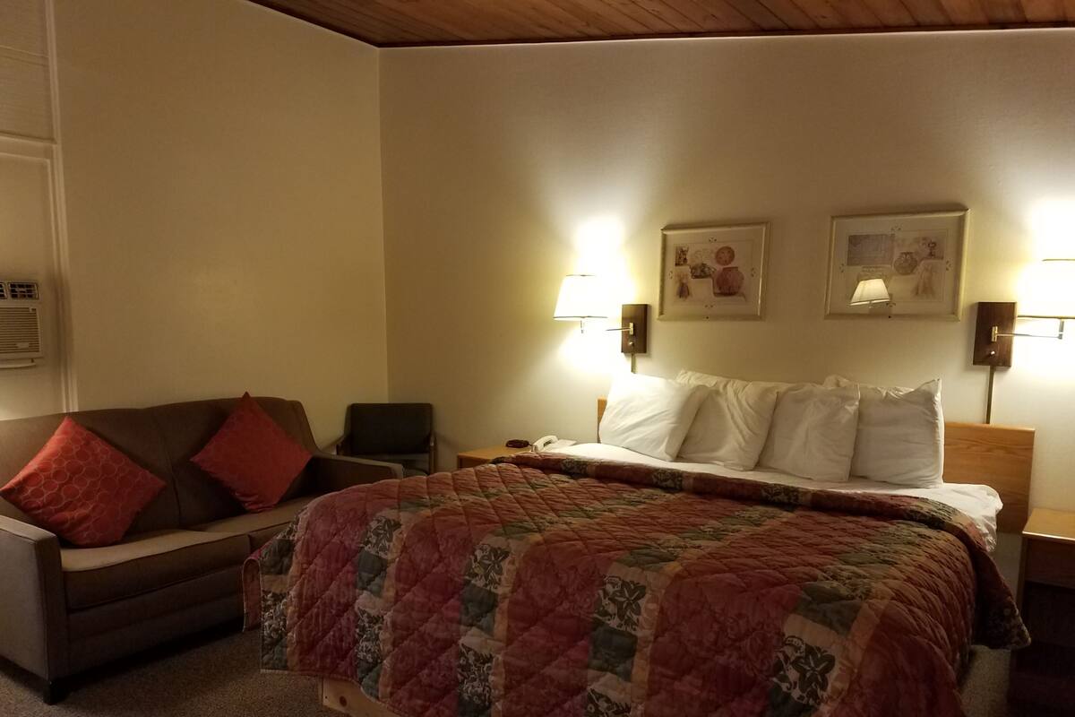 Una habitación de hotel con una cama, una silla, un escritorio y dos lámparas fijadas a la pared.