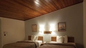 A hotel room with two beds, wooden headboards, a nightstand with a lamp, and wall-mounted artwork.