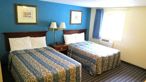 A hotel room with two beds, a nightstand, a lamp, and a window with curtains.