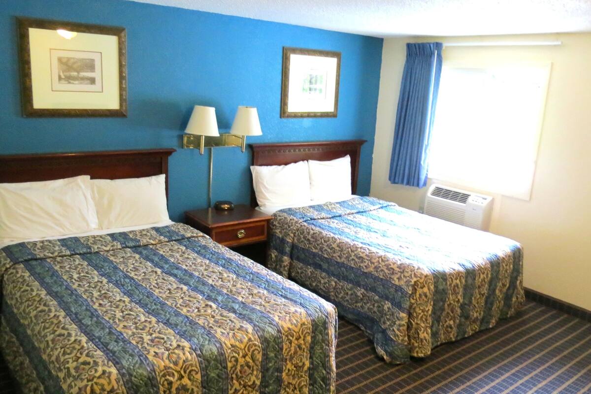 Une chambre d’hôtel avec deux lits, une table de chevet, une lampe et une fenêtre avec des rideaux.