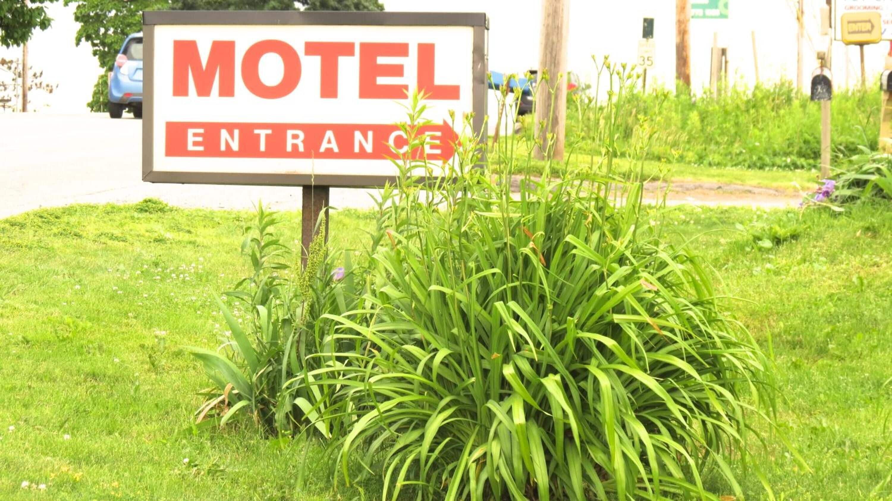 A motel entrance sign with a road and greenery in the background.