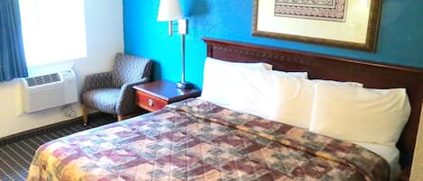 A hotel room with a large bed, a chair, a nightstand, a lamp, and a framed picture on the wall.