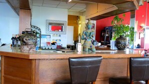 A bar area with a wooden counter, two leather chairs, and decorative items including a statue and a large vase.