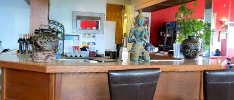 A bar area with a wooden counter, two leather chairs, and decorative items including a statue and a large vase.