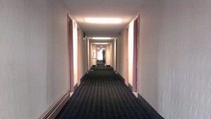 A long, narrow hotel hallway with carpeted floors and doors on both sides.