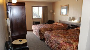 A hotel room with two beds, a desk, a chair, a small table, a telephone, and a window with curtains. - Budget Host Sundowner Motor Inn (Kadoka)