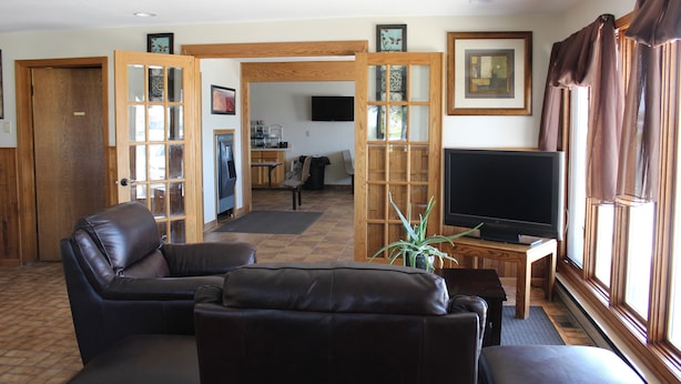 A living room with a leather sofa, a television, and a wooden door leading to another room. - Budget Host Sundowner Motor Inn (Kadoka)