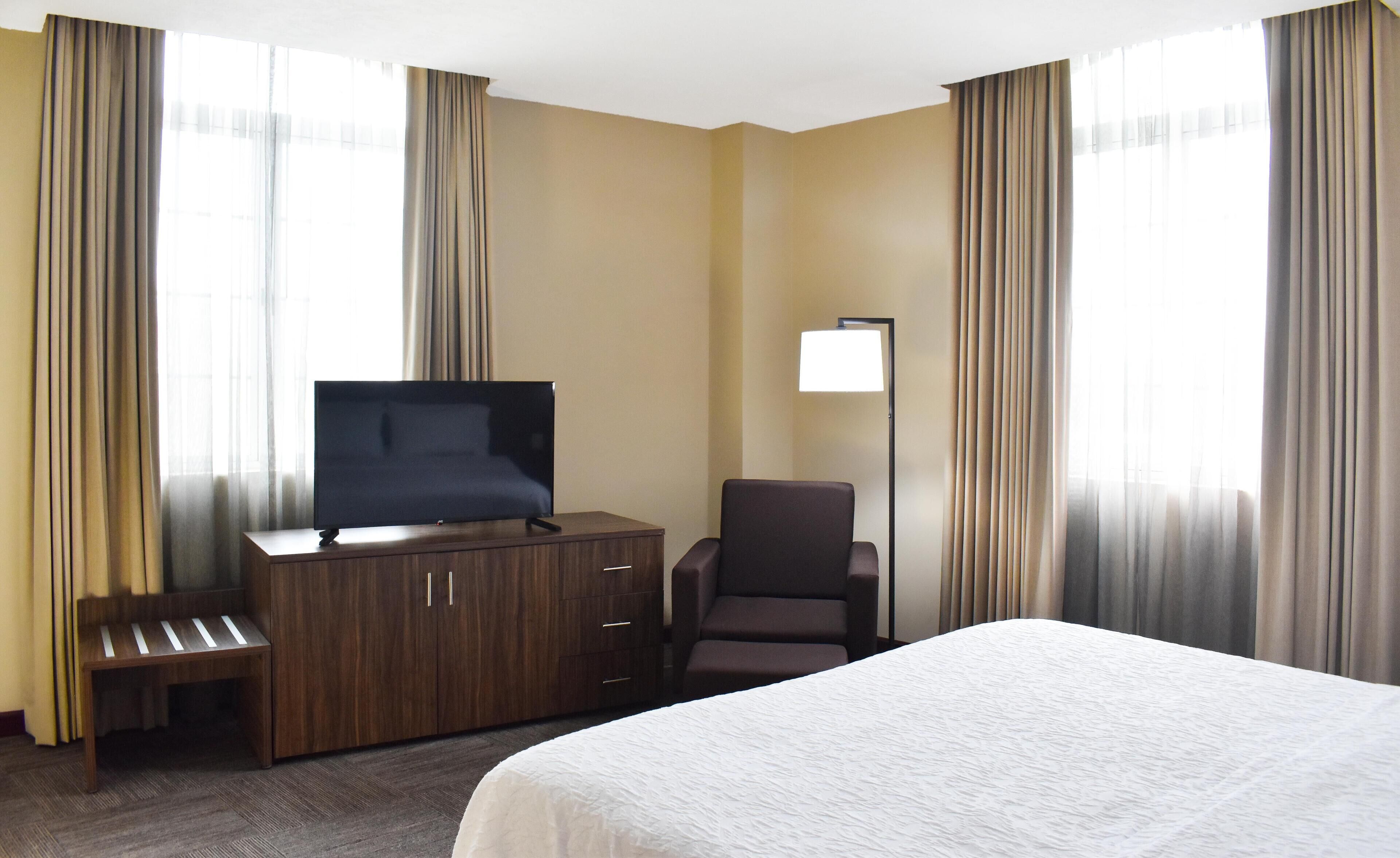 Una habitación de hotel con una cama, un televisor en un mueble de madera, una silla y un escritorio.