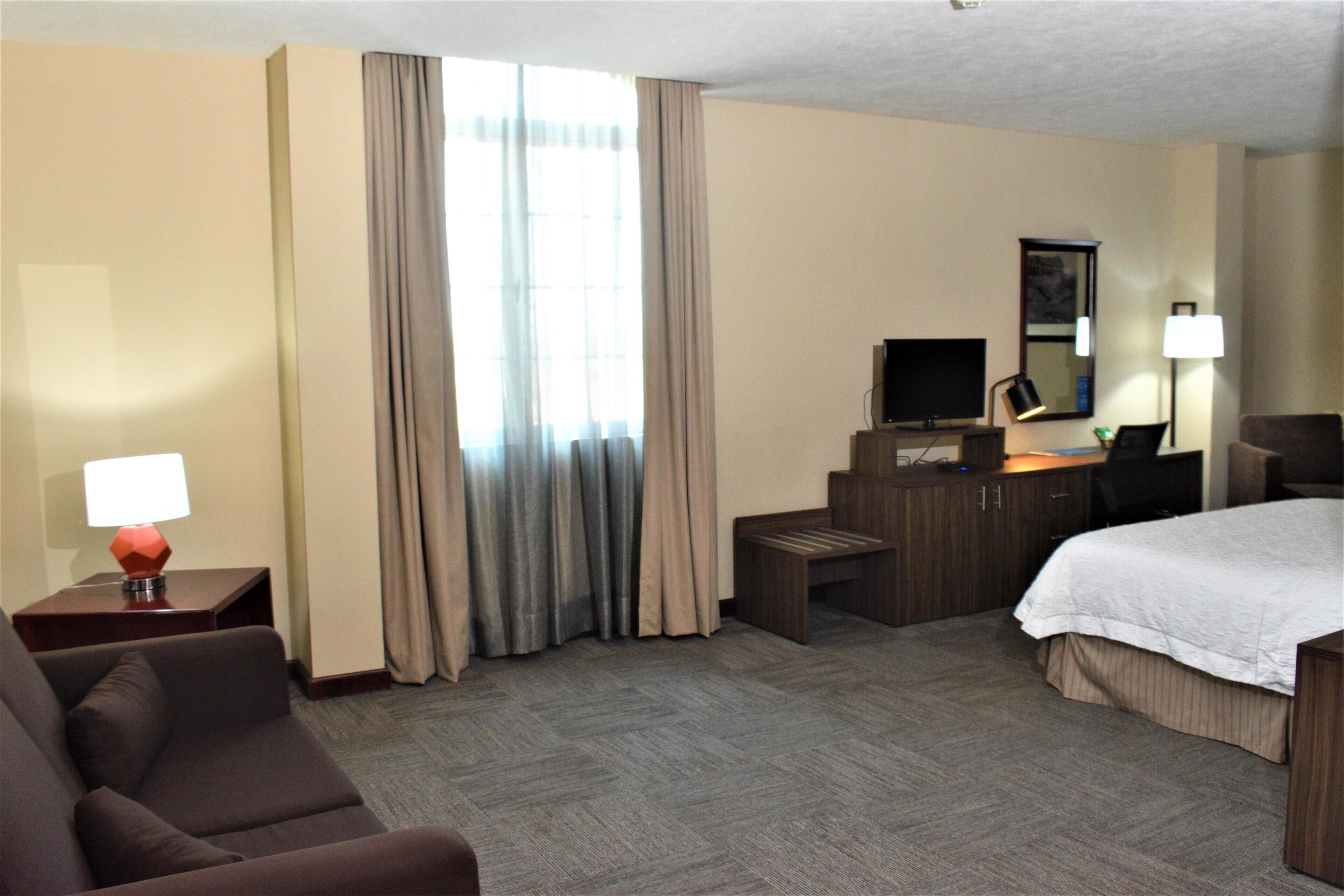 Ein Hotelzimmer mit Bett, Schreibtisch, Fernseher, Lampe und Stuhl.