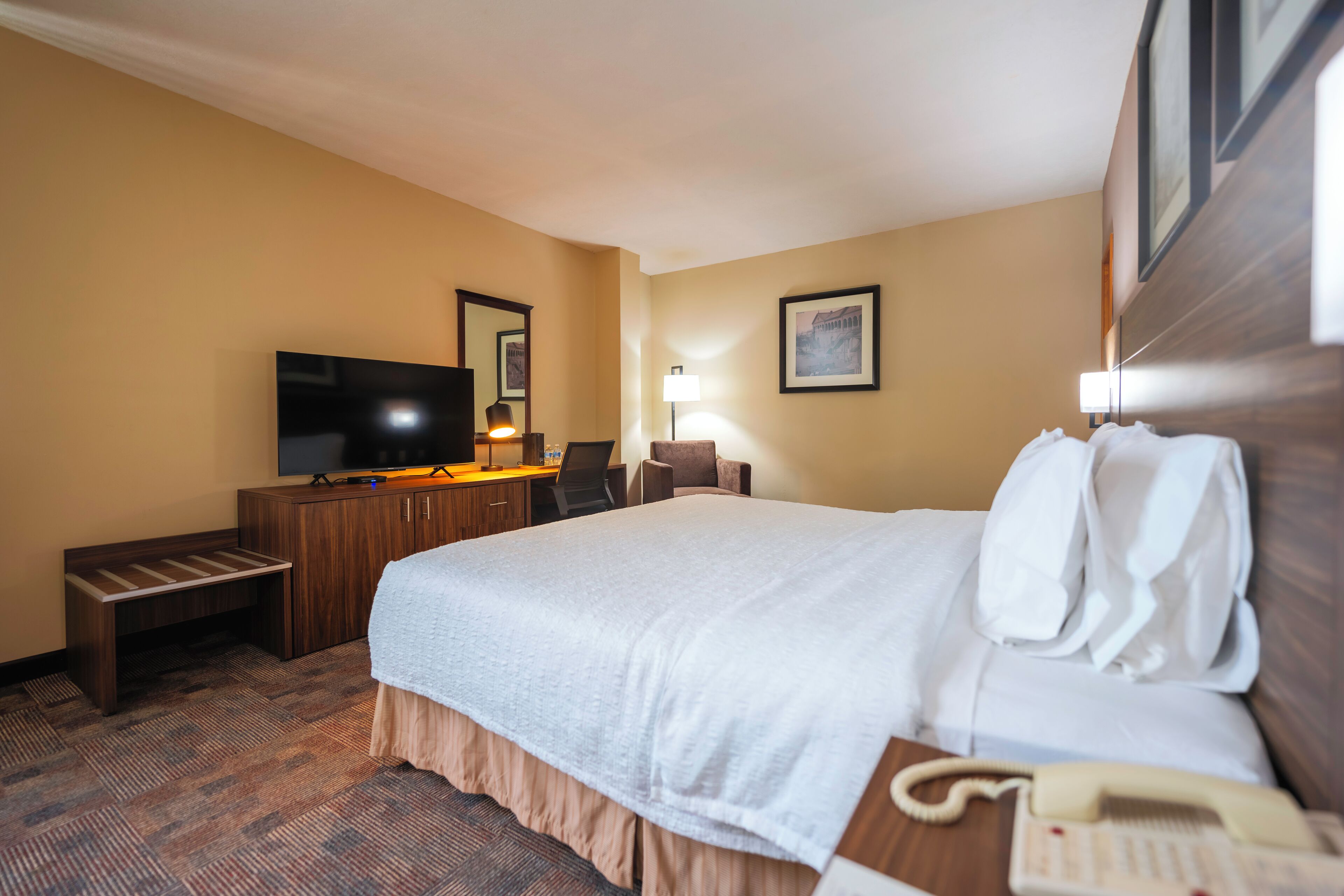Una habitación de hotel con una cama grande, un escritorio con una computadora, un televisor y un teléfono.