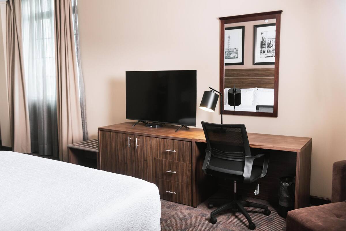 Une chambre d’hôtel avec un lit, un bureau avec un ordinateur, une télévision et une chaise.