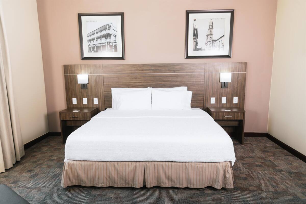 Une chambre d’hôtel avec un grand lit, deux tables de chevet, une tête de lit et deux tableaux encadrés au mur.