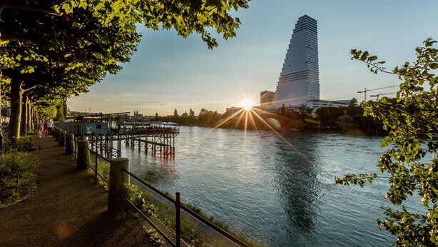 A riverside walkway with a modern building in the background and a bridge extending over the water.
