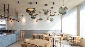 A modern restaurant interior with wooden tables and chairs, hanging pendant lights, and a marble wall.