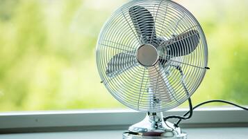 A standing fan with a metal grill and a base, placed on a windowsill.