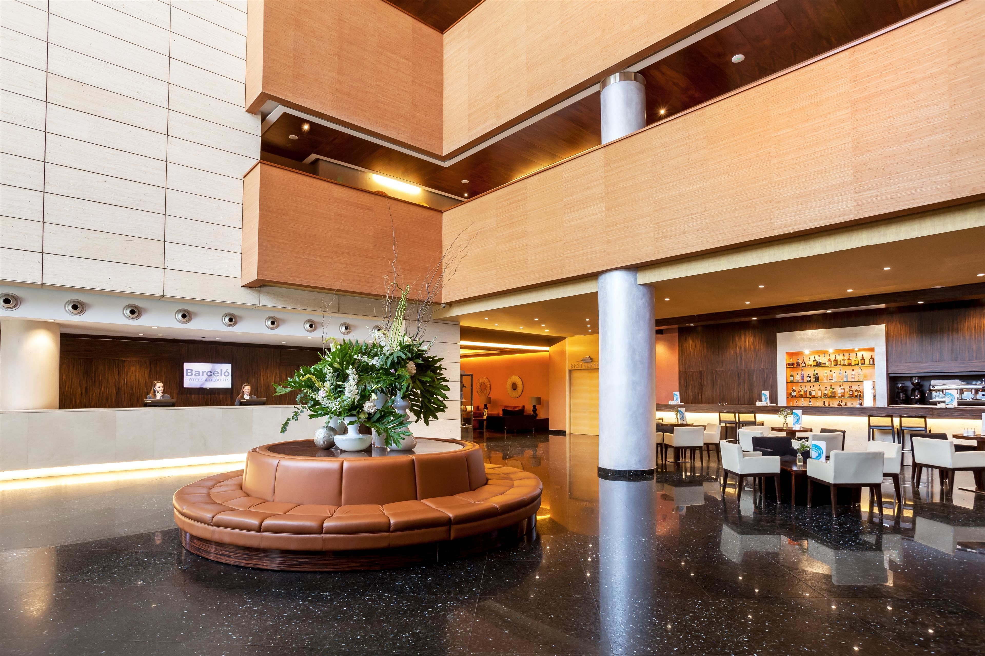 Un vestíbulo moderno con zona de estar central, mostrador de recepción y área de bar/lounge.