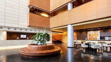 Un vestíbulo moderno con zona de estar central, mostrador de recepción y área de bar/lounge.