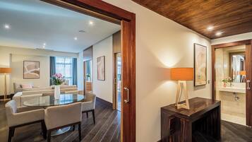 Una habitación de hotel moderna con techo de madera, un área de comedor con mesa de vidrio, un sofá y un baño con lavamanos y espejo.