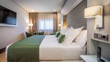 Habitación de hotel con una cama grande, un televisor montado en la pared, una mesita de noche con lámpara y un teléfono también en la pared.