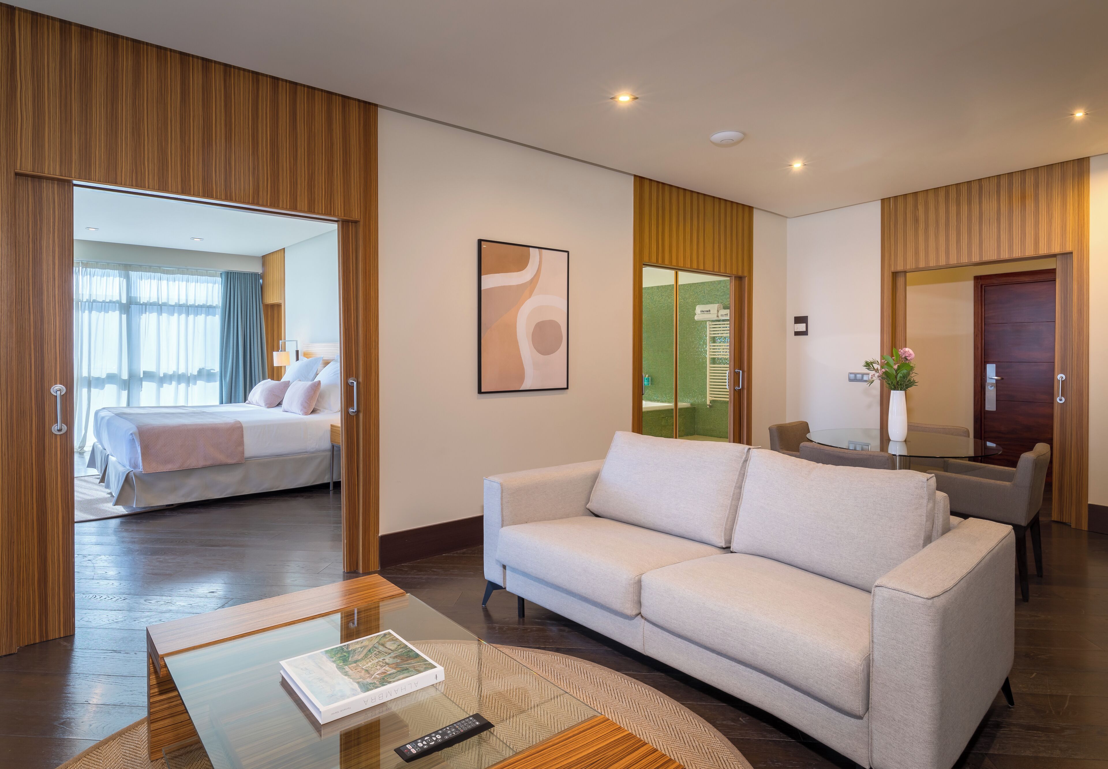 Habitación de hotel moderna con una cama grande, un sofá, una mesita de vidrio y vistas al baño.
