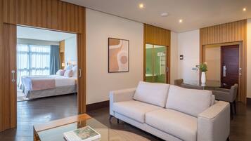 Habitación de hotel moderna con una cama grande, un sofá, una mesita de vidrio y vistas al baño.