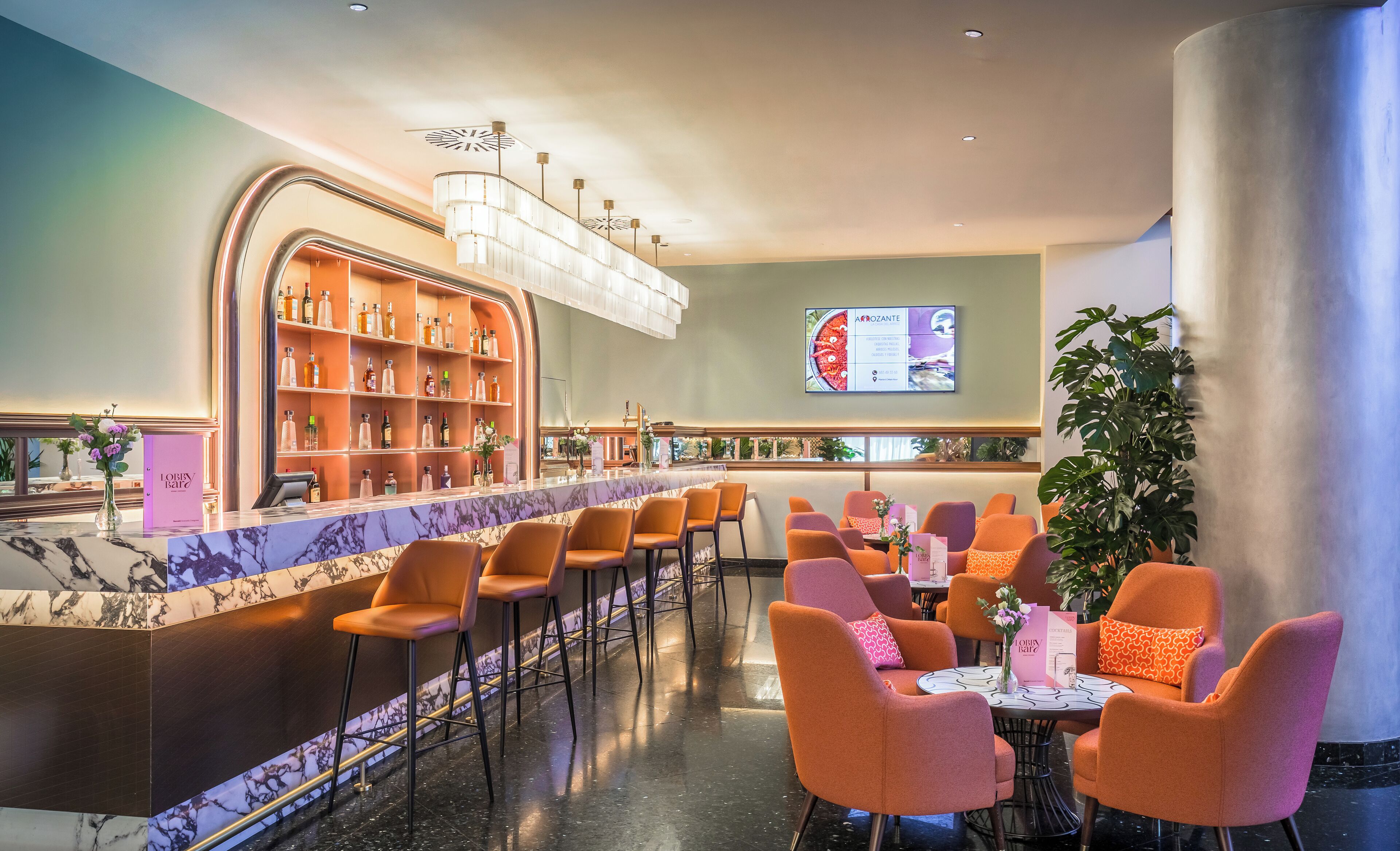 A bar area with a marble counter, orange chairs, and a large plant.