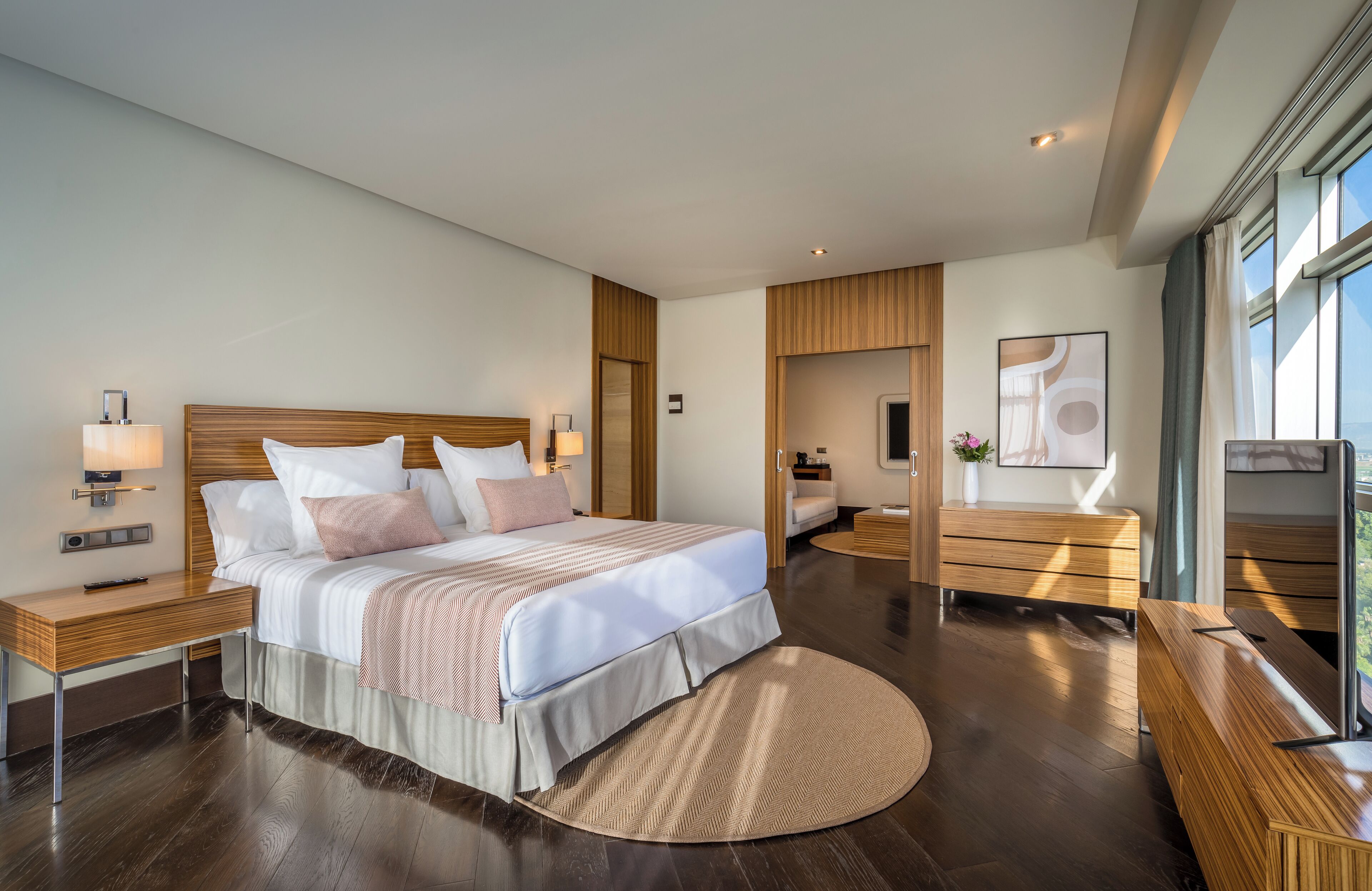 Une chambre d’hôtel moderne dotée d’un grand lit, de tables de chevet, d’un bureau et offrant une vue sur la ville grâce à de grandes fenêtres.