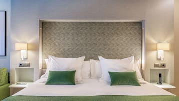 Una cama bien hecha con sábanas blancas y almohadas verdes, un cabecero estampado y lámparas de noche.
