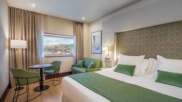 Habitación de hotel con cama, escritorio con dos sillas, ventana que ofrece vistas a la ciudad y pared con diseño.