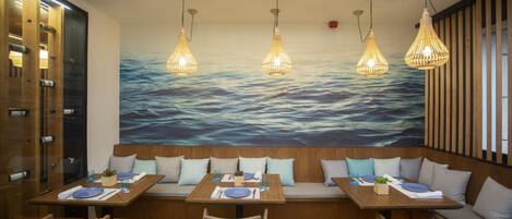 A restaurant with wooden tables and benches, hanging light fixtures, and a large ocean mural on the wall.