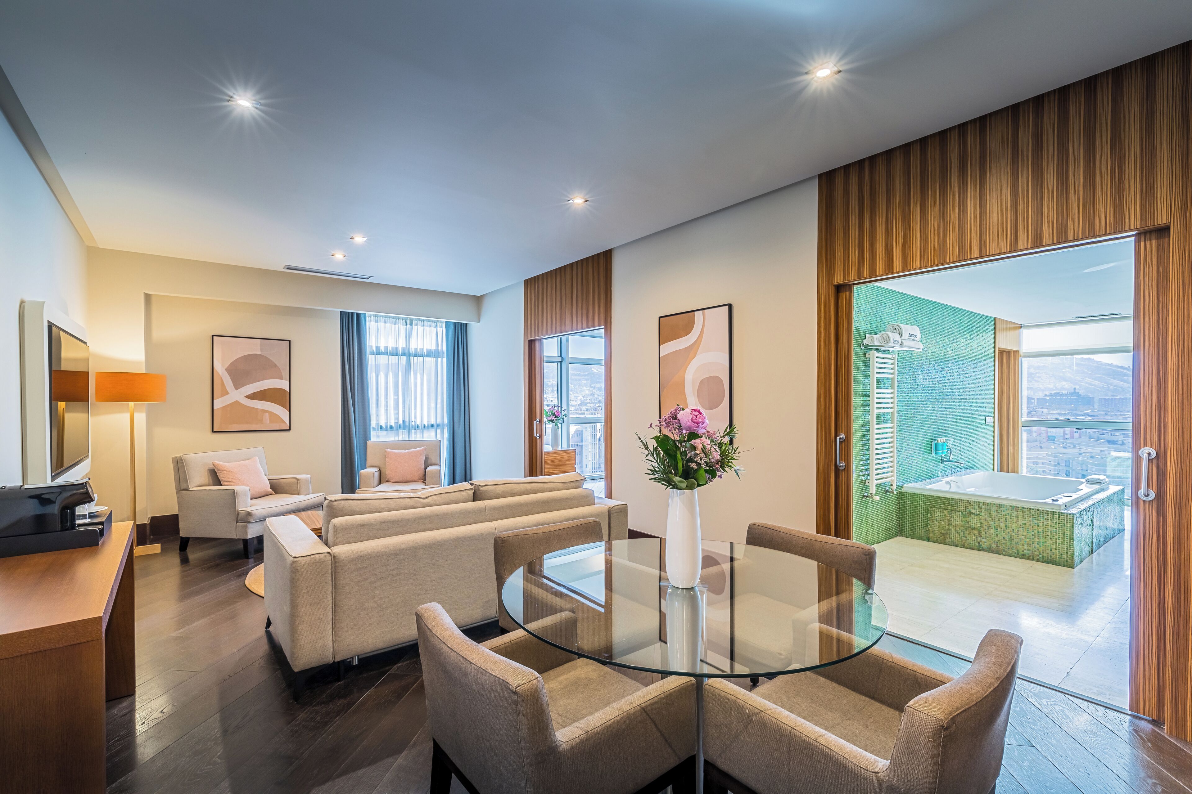 Habitación de hotel moderna con zona de estar, una mesa de vidrio y vistas a la ciudad.
