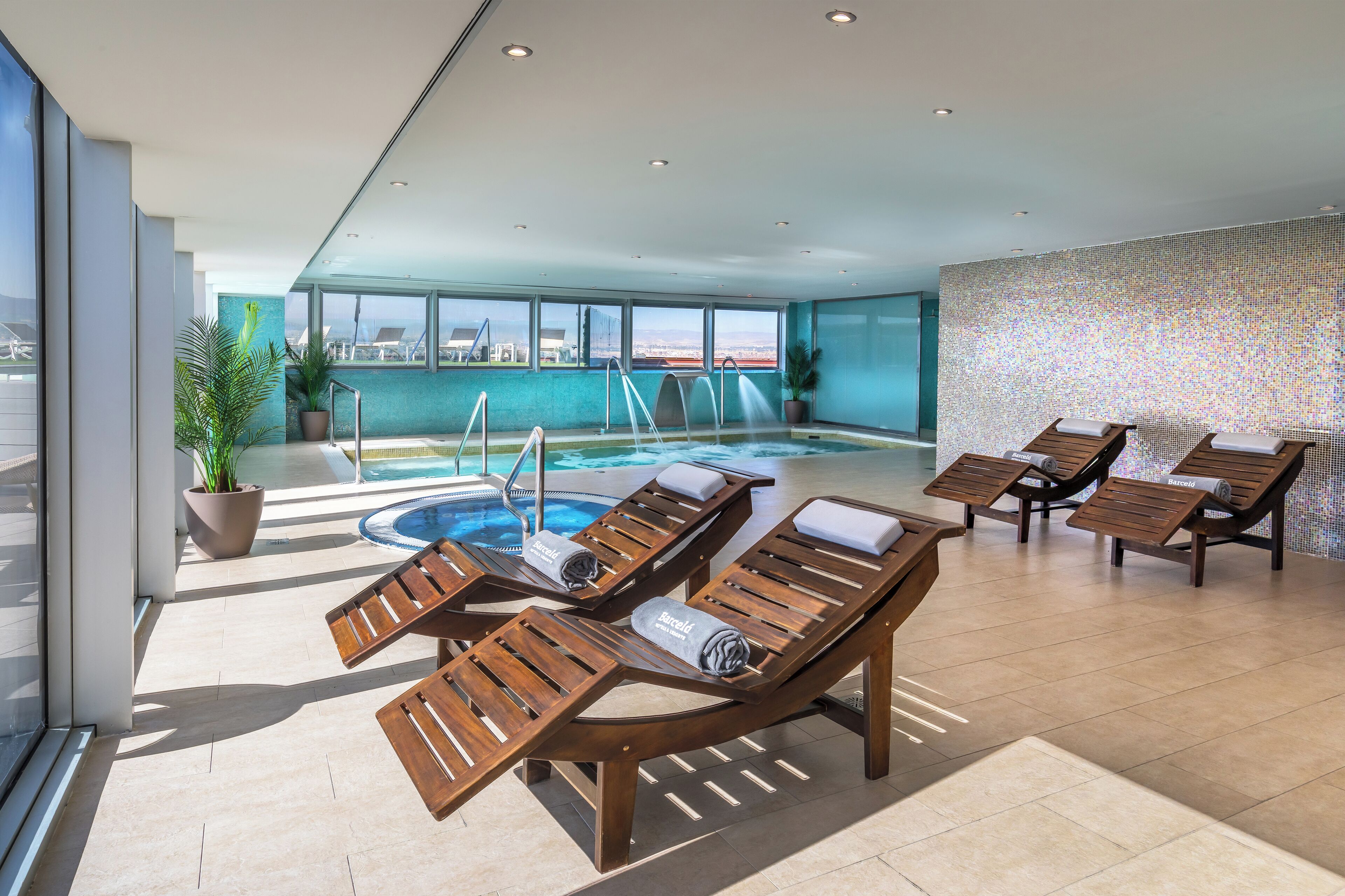 A modern indoor pool area with lounge chairs and a view of the ocean.