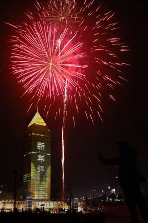 A nighttime view of a cityscape with a prominent tower and fireworks in the sky. - New Century Grand Hotel Hangzhou (Hangzhou)