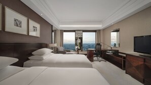 Habitación de hotel con dos camas grandes, un escritorio, televisión y vistas a la ciudad.