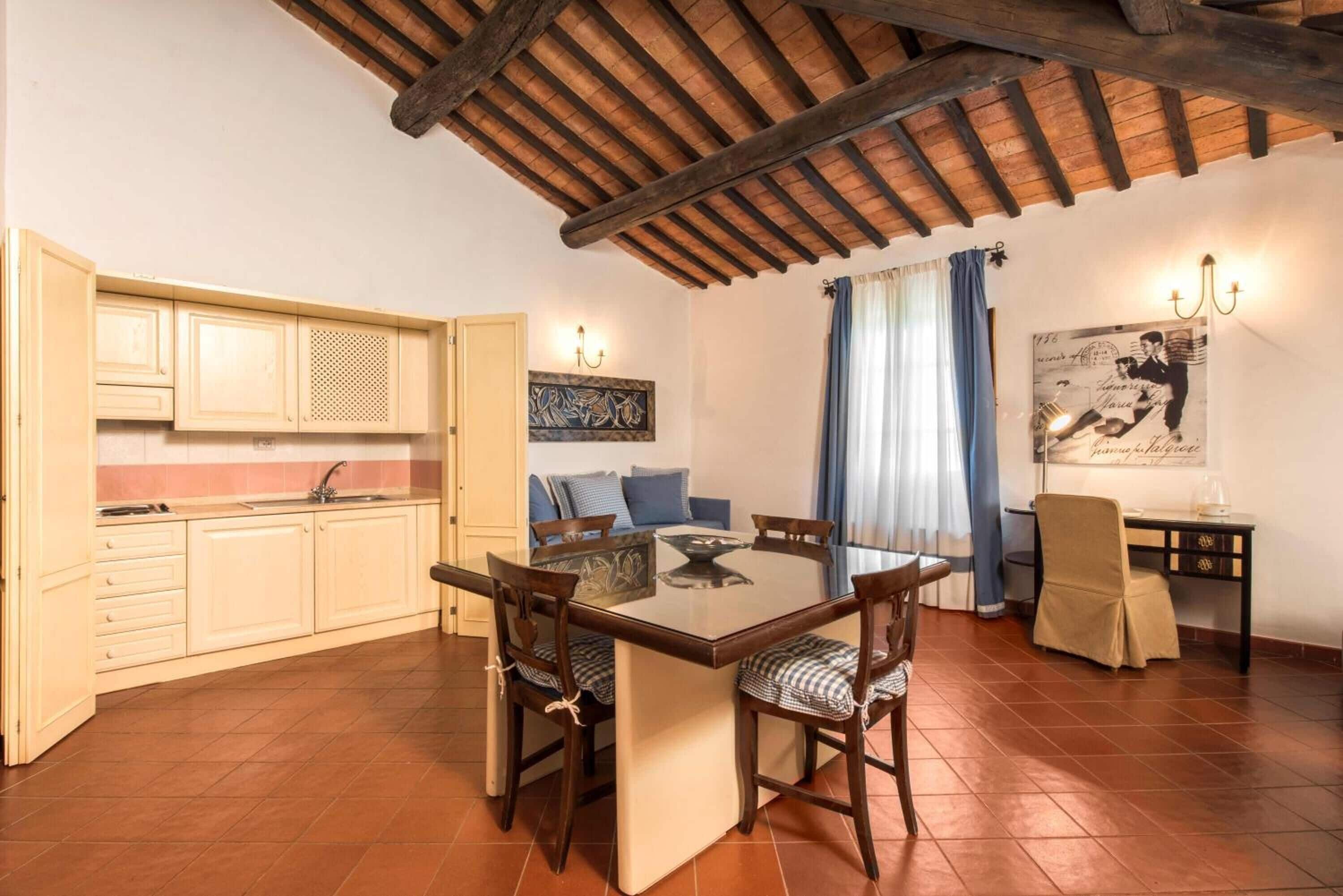 A dining area with a glass-top table, wooden chairs, a sofa, and a kitchen with cabinets and a sink.
