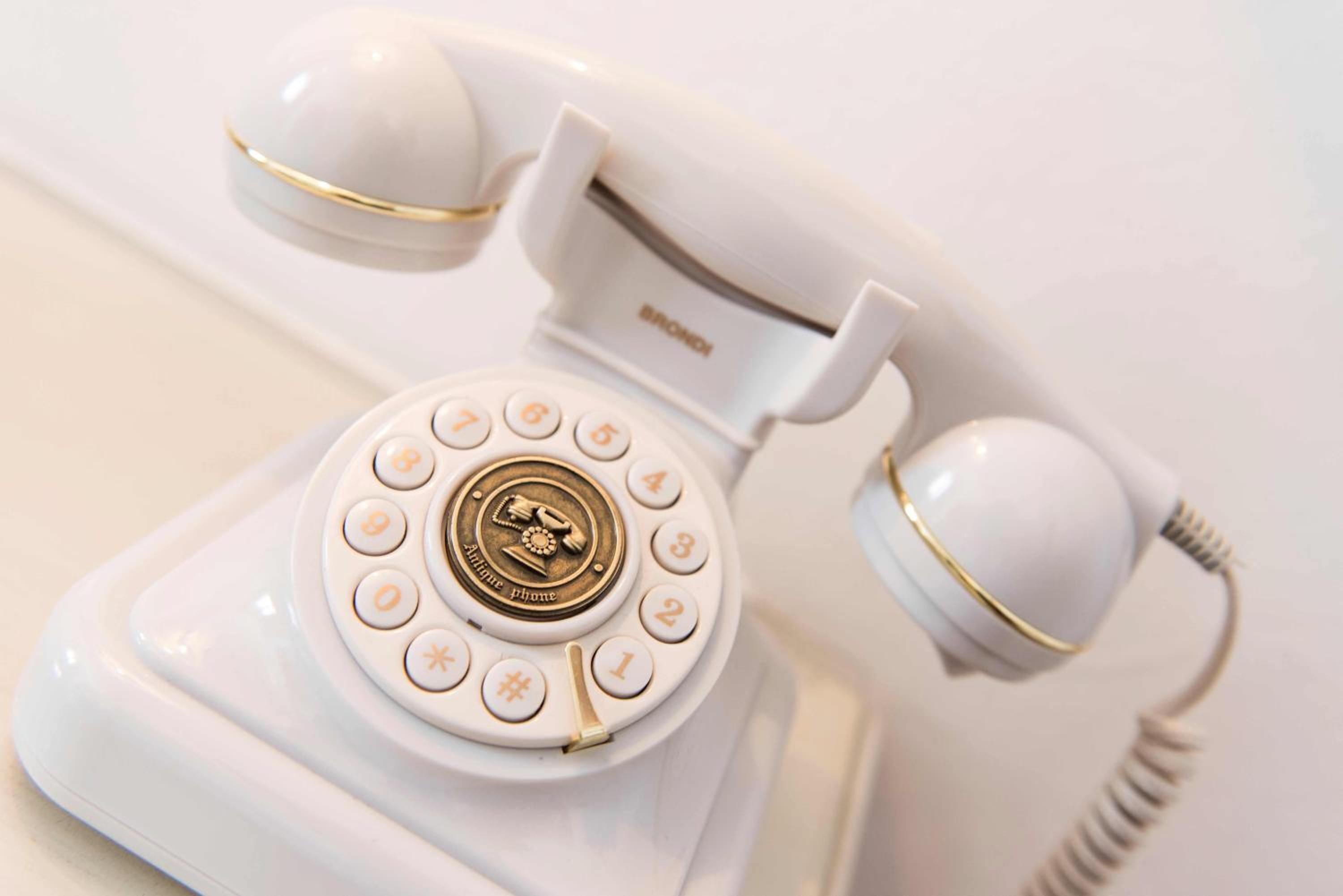 A vintage white rotary dial telephone with gold accents.