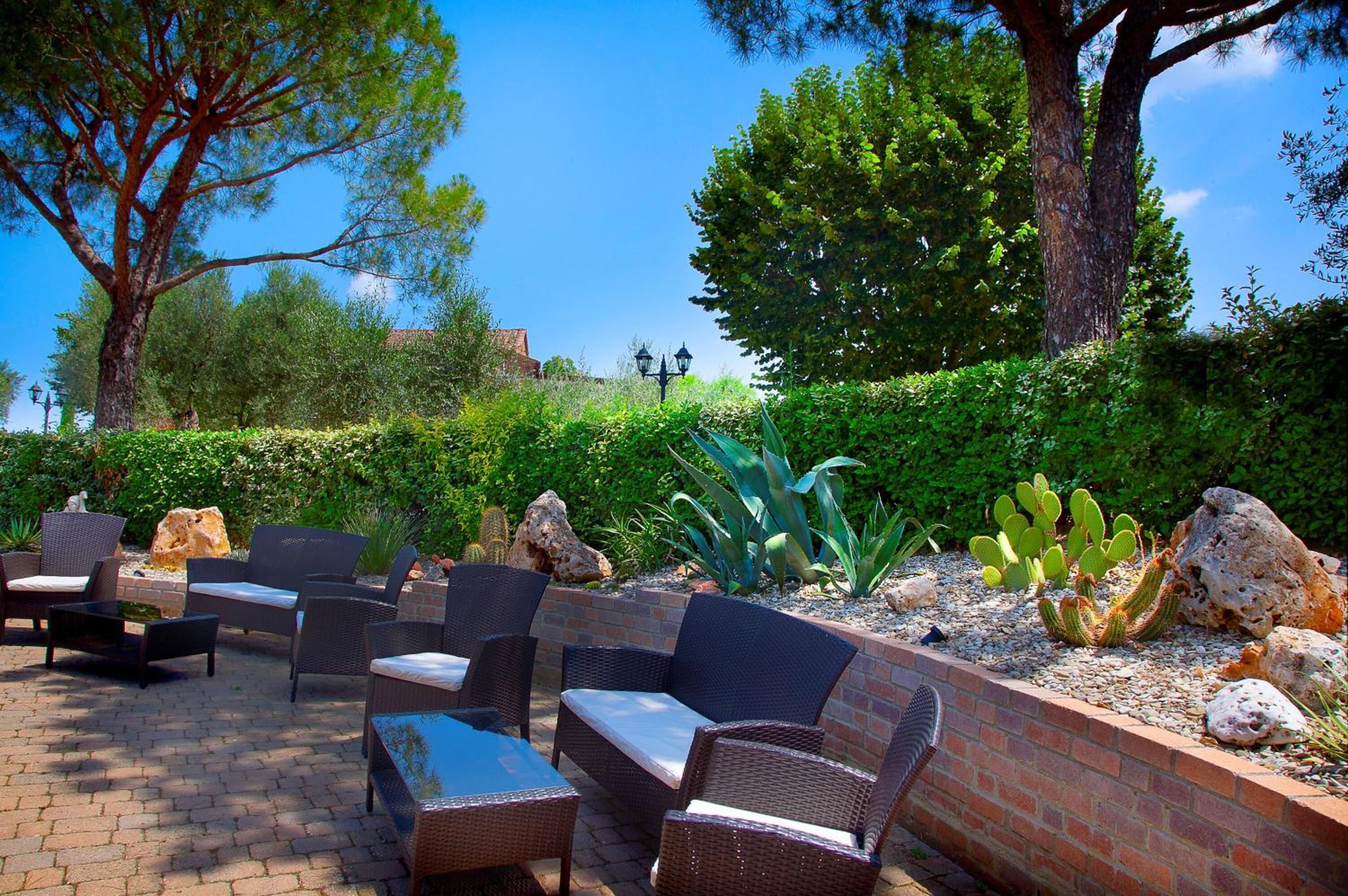 Un espace extérieur aménagé en terrasse, avec des meubles en osier, un mur en briques et des cactus.