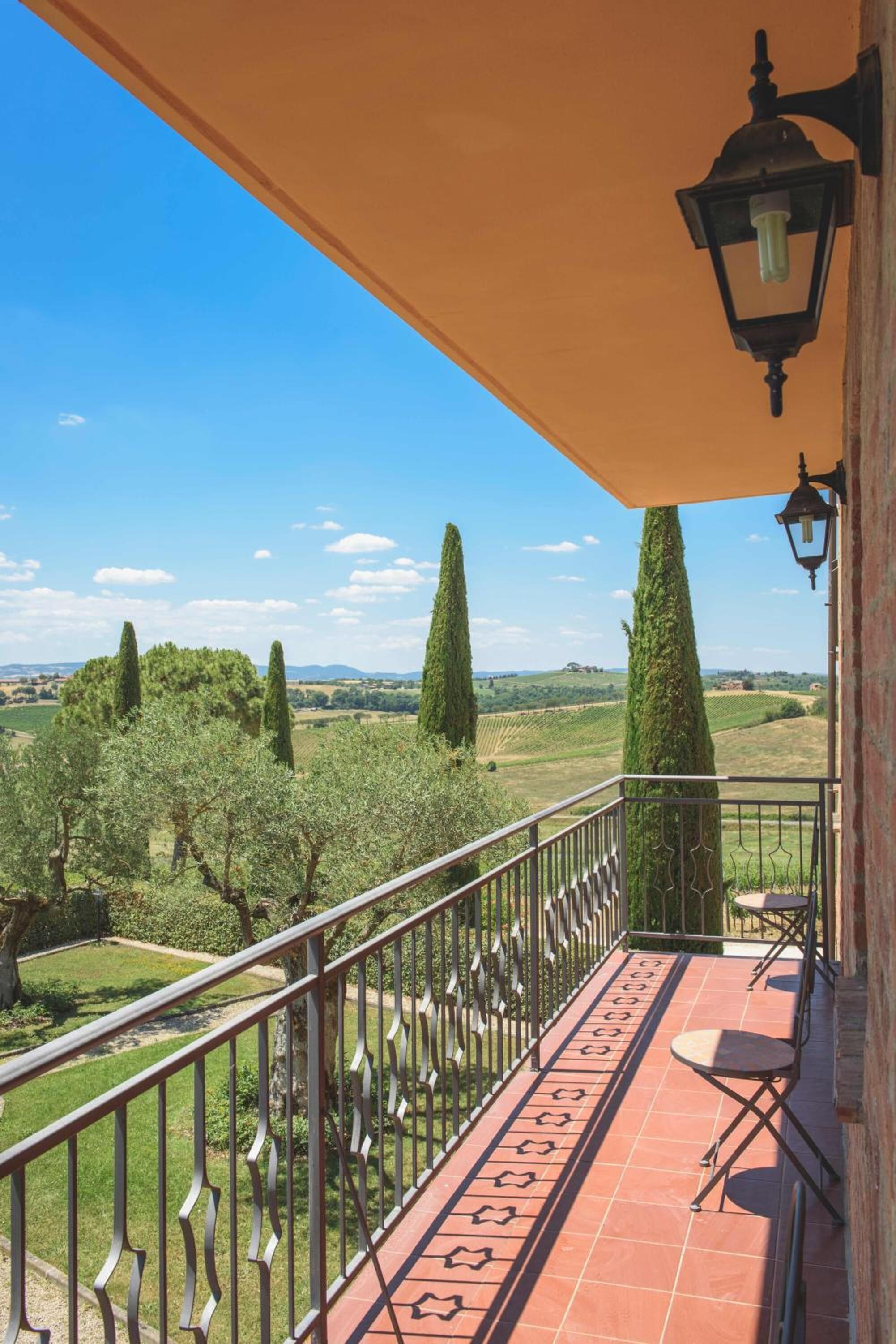 Ein Balkon mit Blick auf einen Weinberg und hohe Bäume, ein Fliesenboden und ein Metallgeländer.