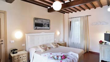 A bedroom with a large bed, bedside tables, a desk with a TV, and a window with curtains.