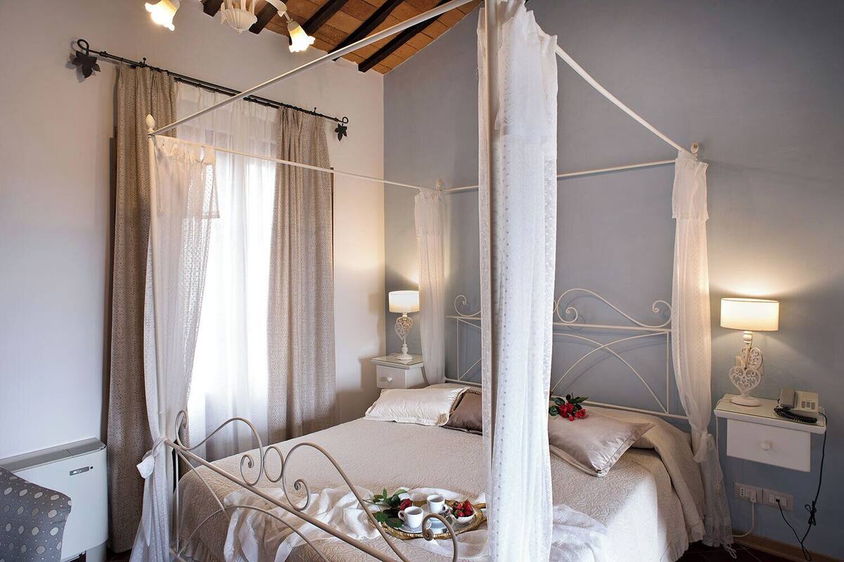 Una cama con dosel y cuatro columnas, dos mesitas de noche con lámparas, un teléfono junto a la cama y una pequeña mesa con un juego de té y flores.