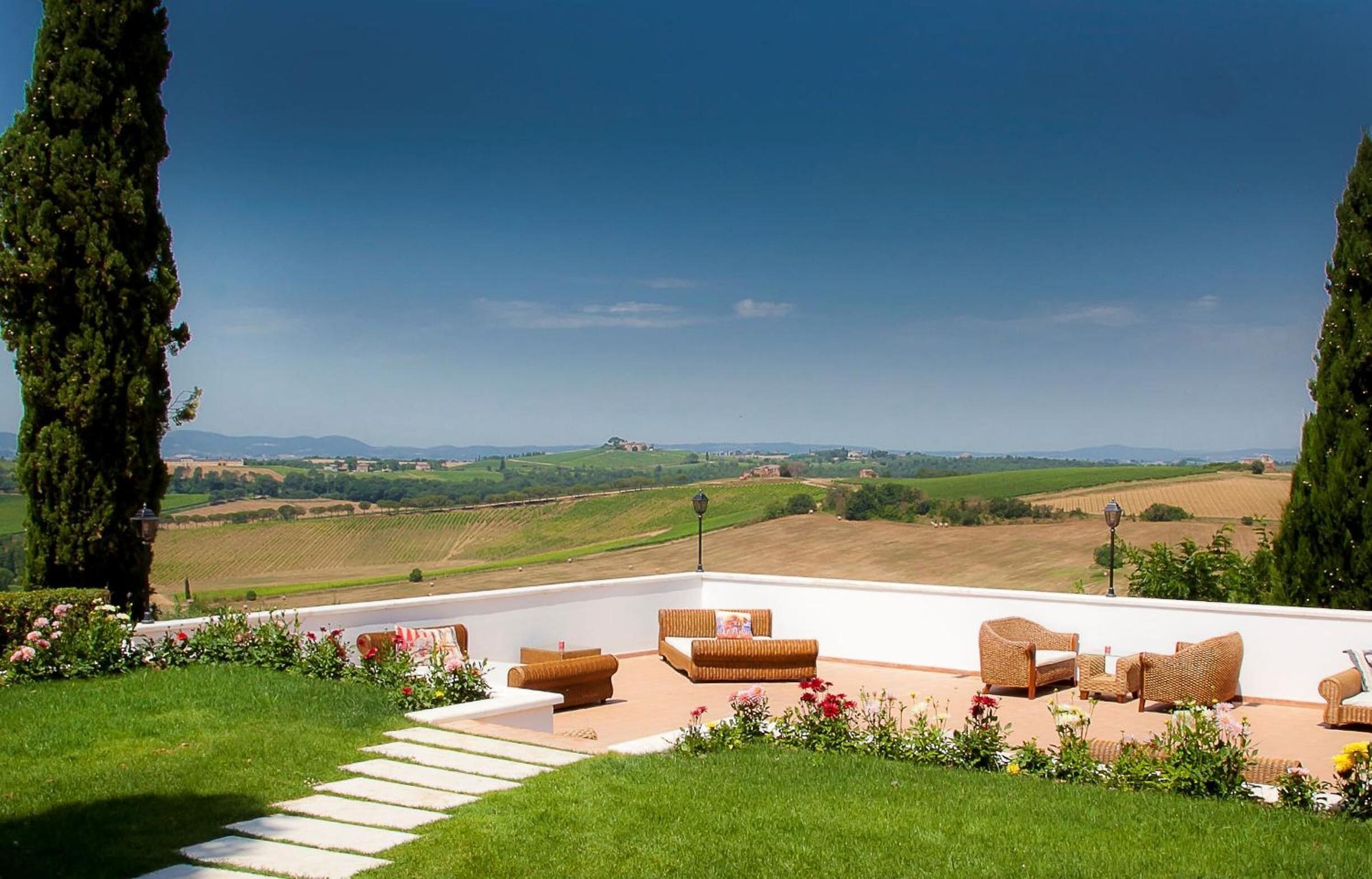 A terrace with wicker furniture and a view of rolling hills.