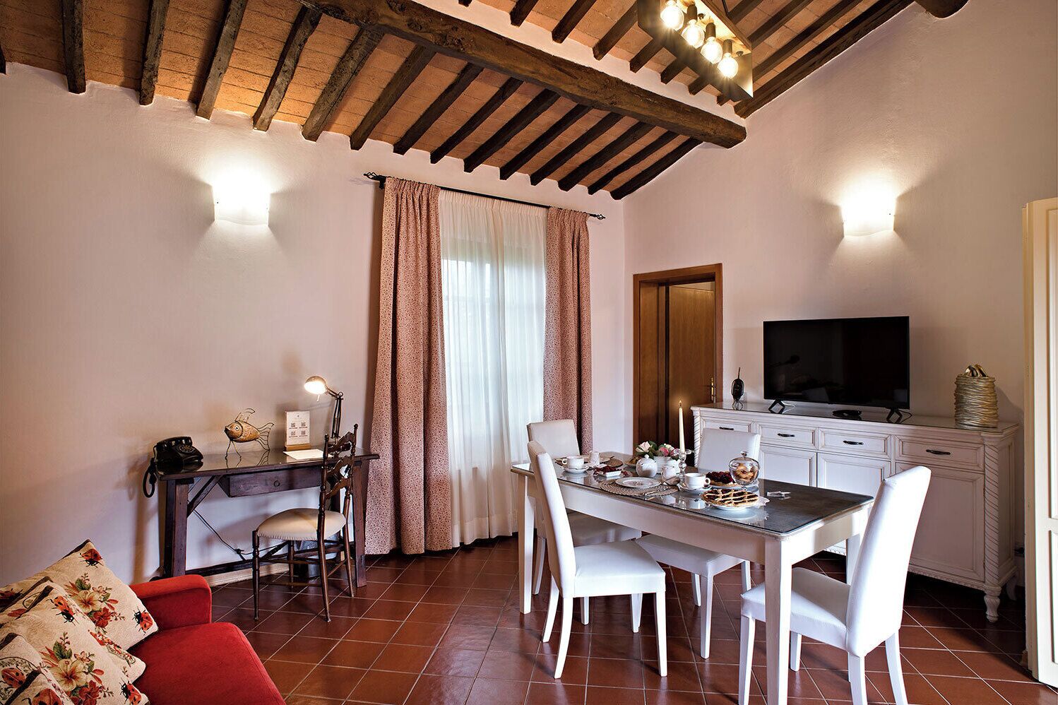 A dining area with a wooden ceiling, a TV on a cabinet, and a table set for two.