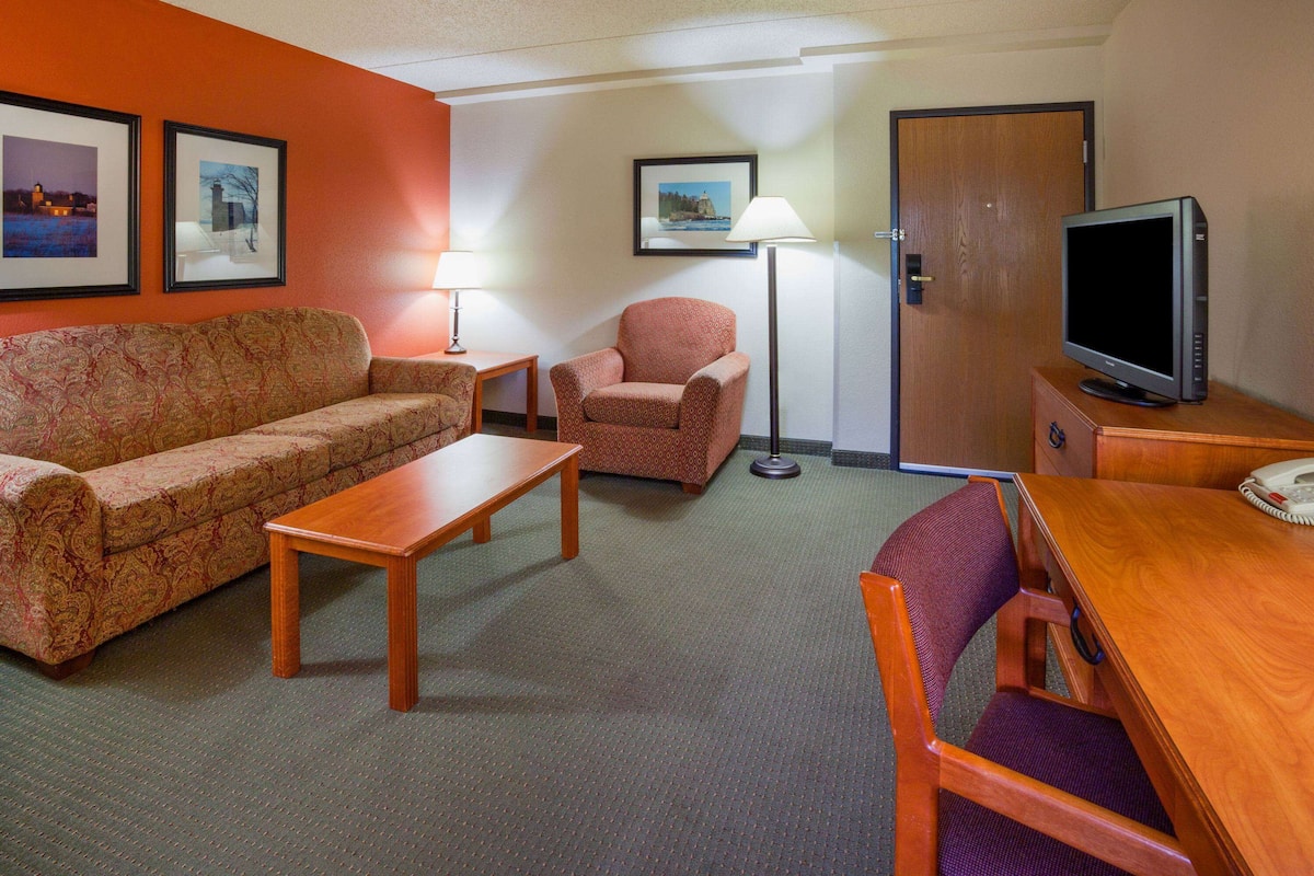 Une chambre d’hôtel équipée d’un canapé, d’un fauteuil, d’une table en bois, d’une lampe, d’une télévision et d’une porte.