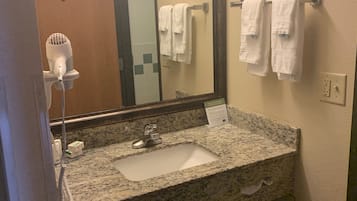Un baño con lavamanos de encimera de granito, un espejo, un secador de pelo y dos toallas colgadas en un perchero.