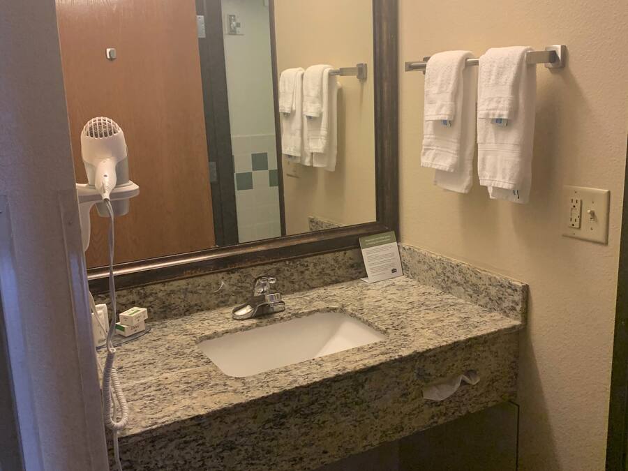Un baño con lavamanos de encimera de granito, un espejo, un secador de pelo y dos toallas colgadas en un perchero.