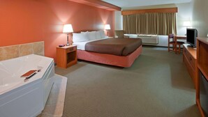 Une chambre d’hôtel avec un grand lit, un bureau avec un ordinateur, une télévision, une salle de bain avec une baignoire et une fenêtre avec des rideaux.