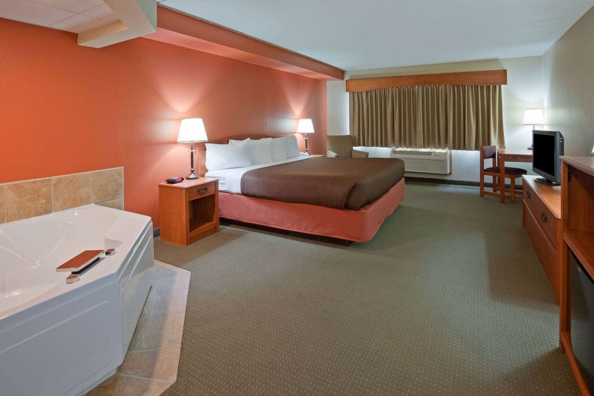 Une chambre d’hôtel avec un grand lit, un bureau avec un ordinateur, une télévision, une salle de bain avec une baignoire et une fenêtre avec des rideaux.