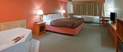 A hotel room with a large bed, a desk with a computer, a TV, a bathroom with a bathtub, and a window with curtains.